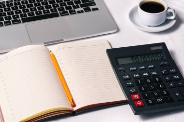 Hesap makinesi, günlük, açık bir dizüstü bilgisayar, bir fincan kahve ve masaüstünde bir defter. Muhasebe, Finans ve İş.