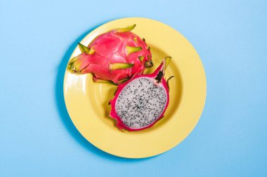 Sarı bir tabakta ejderha meyvesi kes. Renkli arka planda çekirdekleri olan pitaya 'nın altında. Üst görünüm, düz görünüm.