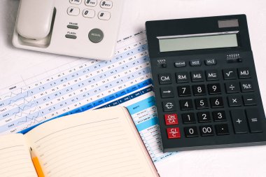 Düğmeye basılı bir telefon, hesap makinesi, bir defter ve tablosu olan bir grafik. Çalışan masasının mali belgeleri. Bir ay ya da bir yıl için rapor ver. Muhasebe, satış ve yatırımlar.