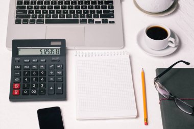 Boş bir Not Defteri, bir fincan kahve, bir bilgisayar ve gözlüğü olan bir şirket çalışanı. Ofiste ya da evde çalış..