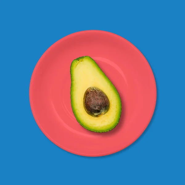 蓝底红盘子里的鳄梨。素食的概念。最小设计艺术. — 图库照片