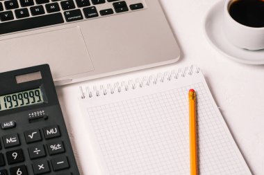 Hesap makinesi, dizüstü bilgisayar, bir fincan kahve ve kalemle birlikte bir defter. Metin için boş sayfa. Muhasebe, yatırım veya bankacılık