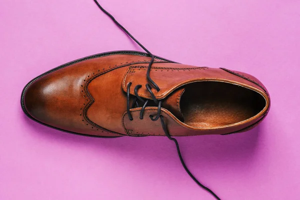 Brown shoes on a colored background with untied laces. Fashionable classic leather shoes. Men's style. The view from the top.