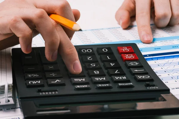 Calculator and hands with a pencil. Desktop with financial and accounting documents. Person counts on a calculator and analyzes the data