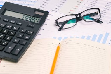 Günlük, gözlükler ve hesap makinesi çalışma masasında. Grafikleri ve numaraları olan iş adamları masaüstü bilgisayarı. Muhasebe, danışmanlık ve pazarlama analizi.