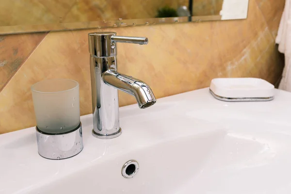 Grifo de cromo y fregadero blanco. Interior de un baño en una casa u hotel. El concepto de lavado de manos y protección contra virus —  Fotos de Stock