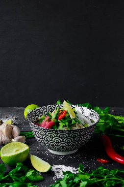 Pho Bo Vietnamca çorbası erişte, sığır eti, chili biber, soğan, kişniş ve kopya alanı üst ile koyu siyah arka plan üzerine kireç