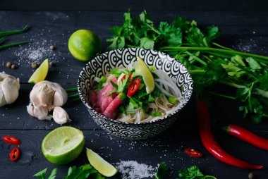 Pho Bo Vietnamca çorbası erişte, sığır eti, chili biber, soğan, kişniş ve limon koyu siyah arka plan üzerine