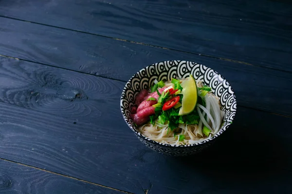 Pho Bo Vietnamca çorbası erişte, sığır eti, chili biber, soğan, kişniş ve limon koyu siyah arka plan üzerine