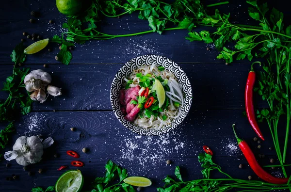 Pho Bo Vietnamca çorbası erişte, sığır eti, chili biber, soğan, kişniş ve limon koyu siyah arka plan üzerine