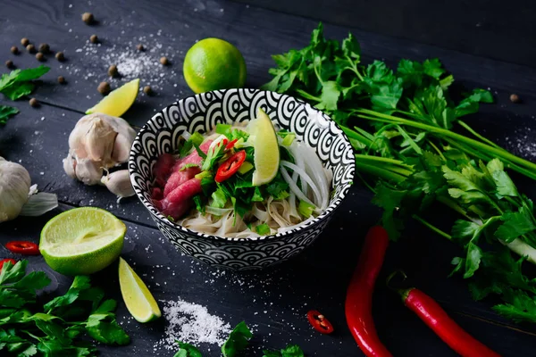 Pho Bo Vietnamca çorbası erişte, sığır eti, chili biber, soğan, kişniş ve limon koyu siyah arka plan üzerine