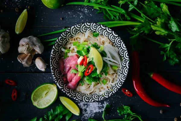 Pho Bo Vietnamca çorbası erişte, sığır eti, chili biber, soğan, kişniş ve limon koyu siyah arka plan üzerine