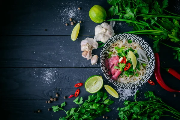 Pho Bo Vietnamca çorbası erişte, sığır eti, chili biber, soğan, kişniş ve limon koyu siyah arka plan üzerine