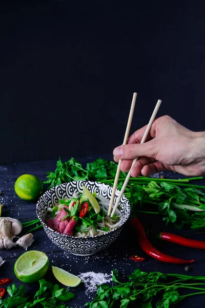 Pho Bo Vietnamca çorbası erişte, sığır eti, chili biber, soğan, kişniş ve limon el ile koyu mavi ahşap arka plan üzerinde