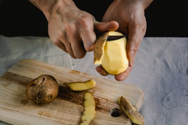 Şef patates temizler. Patates ile yemekler için. Siyah bir arka plan, menü, yemek, sağlıklı beslenme kavramı 