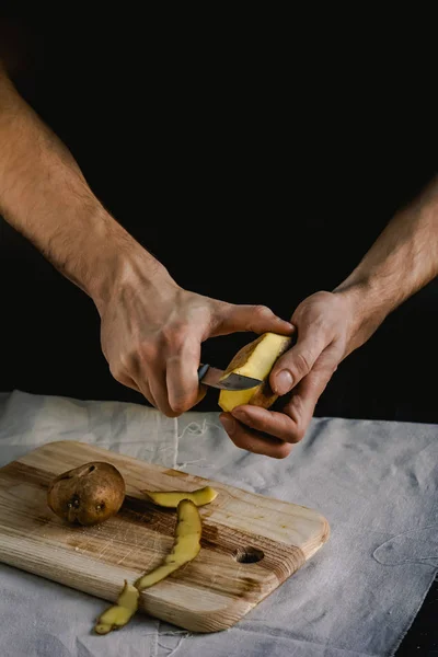 Şef patates temizler. Patates ile yemekler için. Siyah bir arka plan, menü, yemek, sağlıklı beslenme kavramı 