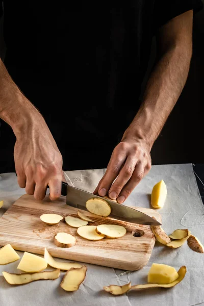 Şefin eli, masada yemek pişirmek için taze ve lezzetli patatesleri kesiyor. Sağlıklı gıda.