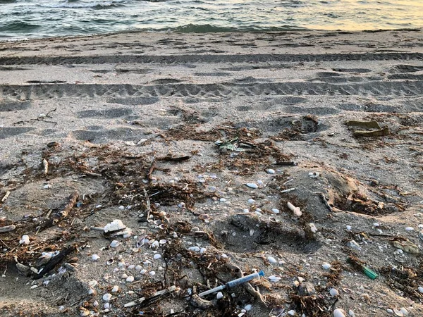 Medyczne strzykawki wśród rapan muszli w piasku na plaży po burzy — Zdjęcie stockowe