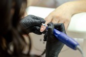Maniküre Pediküre Verfahren Meister macht Sägemaschine von Hand in schwarzen Handschuhen, Nanosc-Nagellack, verschiedene Winkel, Hautcreme erweicht Massage, Frauenhände