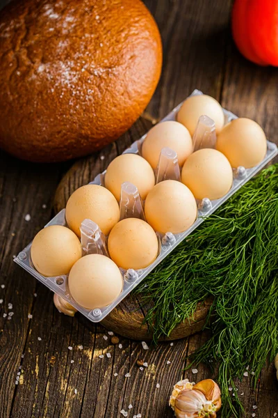 chicken eggs in a package on a wooden board, spices and coarse salt, rustic style, greens, a cherry tomato branch, on a black background