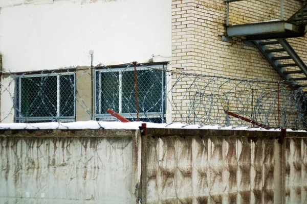 Bakstenen gebouw met bars op de ramen van de betonnen omheining met prikkeldraad — Stockfoto