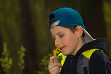 Beysbol şapkalı bir çocuk ormanda sarı bir çiçek salar..
