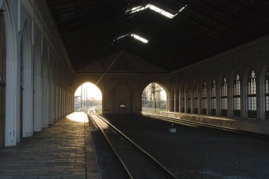 İstasyonun çatısı altında demiryolu rayları. Güneşin ışığı duvardaki kemerlerden geçer. Yolculuk öncesi trenin gelmesini bekliyorum.