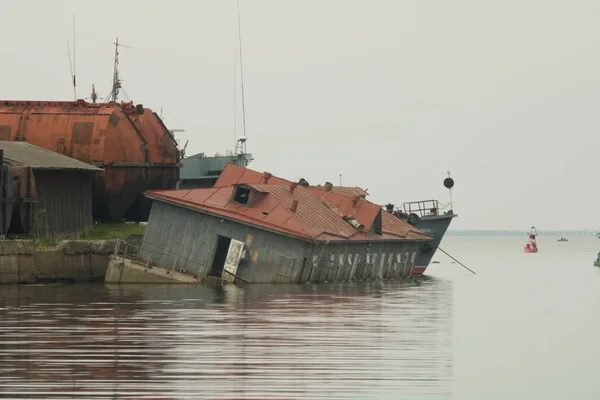 Το ξύλινο κτήριο με την κόκκινη στέγη στο νερό του κόλπου βυθίστηκε μερικώς. Η κατεστραμμένη δομή κεκλιμένη. Royalty Free Εικόνες Αρχείου