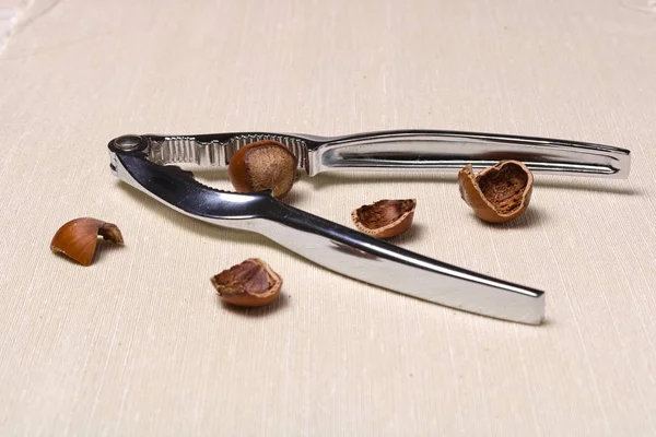Kovové ořechy kleště a vegetariánské potraviny lískových oříšků na hrubé látky zblízka — Stock fotografie