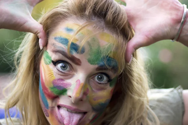 Attractive woman with multi colored face in the public park making a silly face