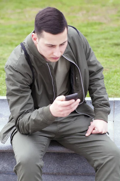 Portrait of young handsome guy texting sms in public park