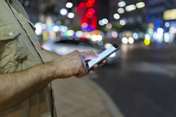 Close up View of Smart Phone in Male Hand in the City Streets with Illuminated Lights in Background