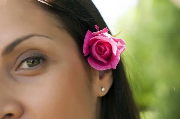 Portrait of attractive black haired woman with rose in her hair outdoors