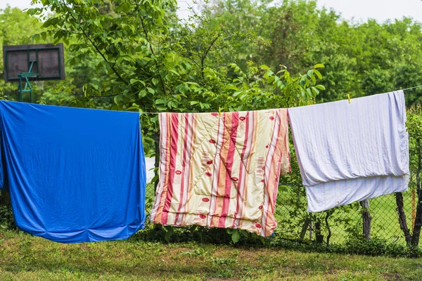 Dry blankets after washing in the sun on a wire in the garden outside the house