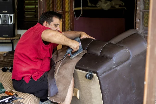 Man upholstering a round stool seat