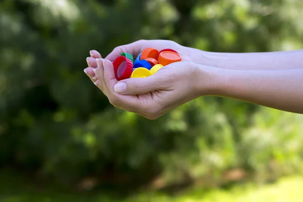 Close up view of female hands in nature holding plastic caps in multi color