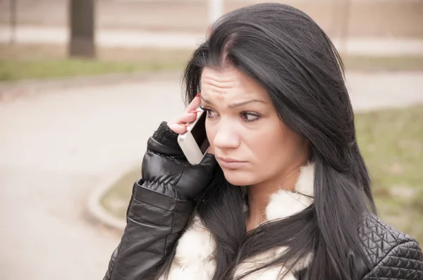 Smiling young woman using phone in park at cold winter day