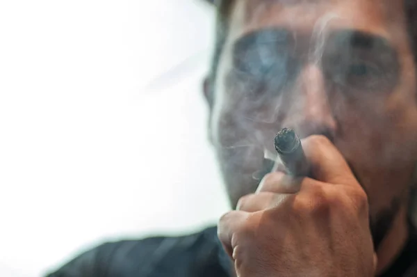 Closeup face in profile of man with burning cigar in mouth.