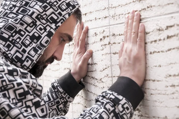 Young depressed man suffering from anxiety and feeling miserable cover his face with his hands and cry leaning on the wall