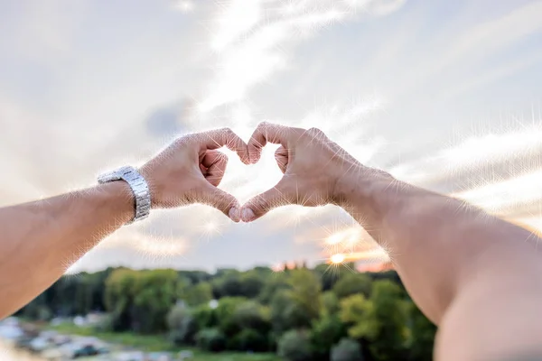 Human hands making Heart shaped sign over sunset sky.