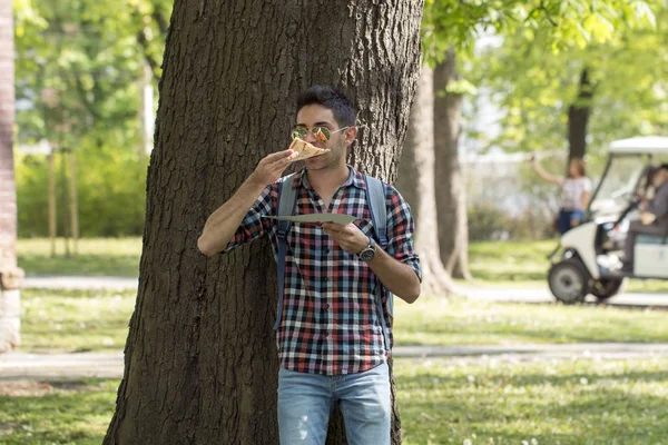 handsome young man eats a pizza in the park