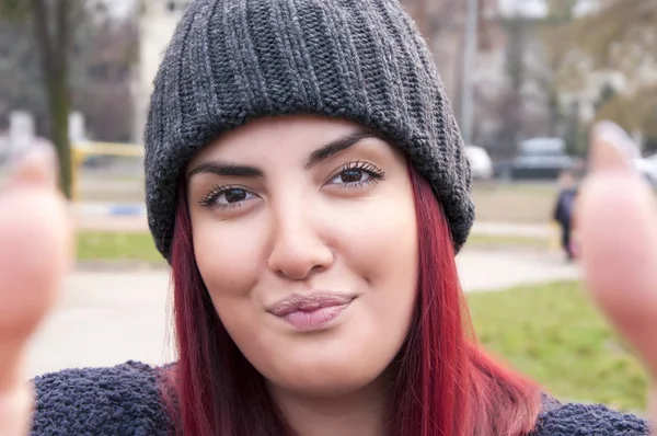 Seductive young redhead with woolen hat taking a selfie photo in the public park