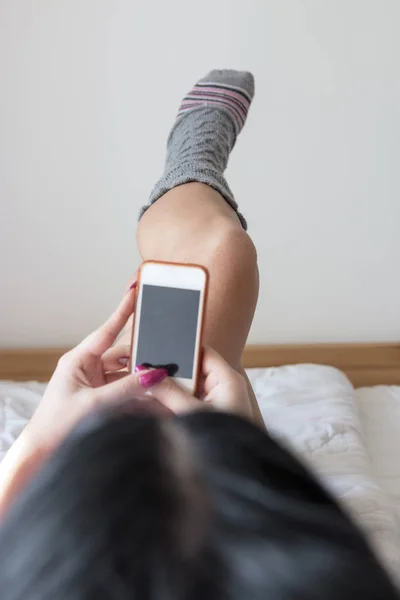 Woman with perfect waxed legs pointing up watching beauty advertising on line with smart phone lying on a bed at home or hotel room
