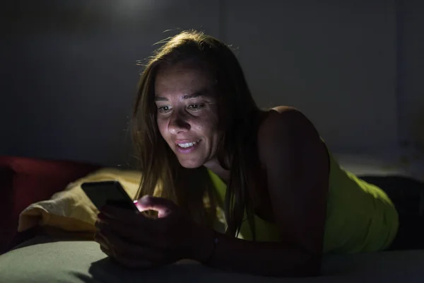 Young woman with smartphone in bed at home bedroom