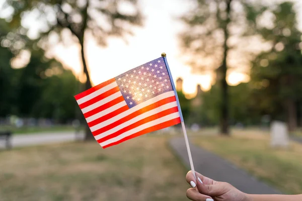 Woman hand is waving US flag outdoors on the Independance day.