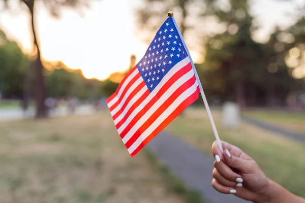 Woman hand is waving US flag outdoors on the Independance day.