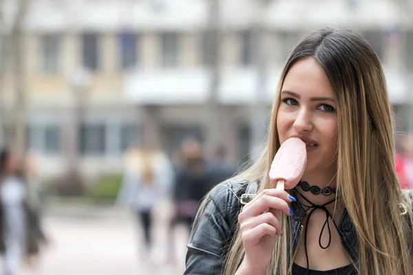 Friendly woman dressed in leather jacket  enjoy her ice cream on the street. She shows ice cream at camera with fantastic great smile, truly emotions, focus on ice cream