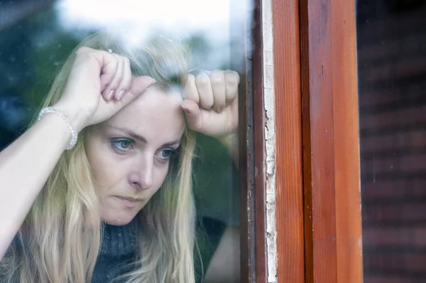 Sad and anxious beautiful woman is worried and looking through the window