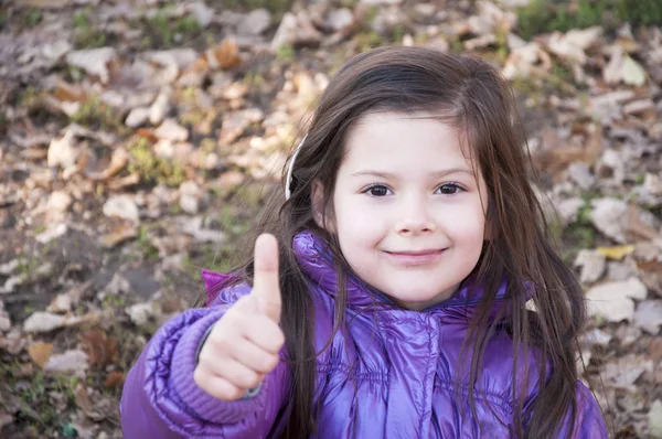 Sweet little girl in purple jacket and woolen purple hat having fun in the playground