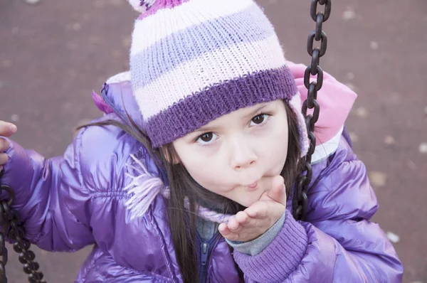 Sweet little girl in purple jacket and woolen purple hat having fun in the playground